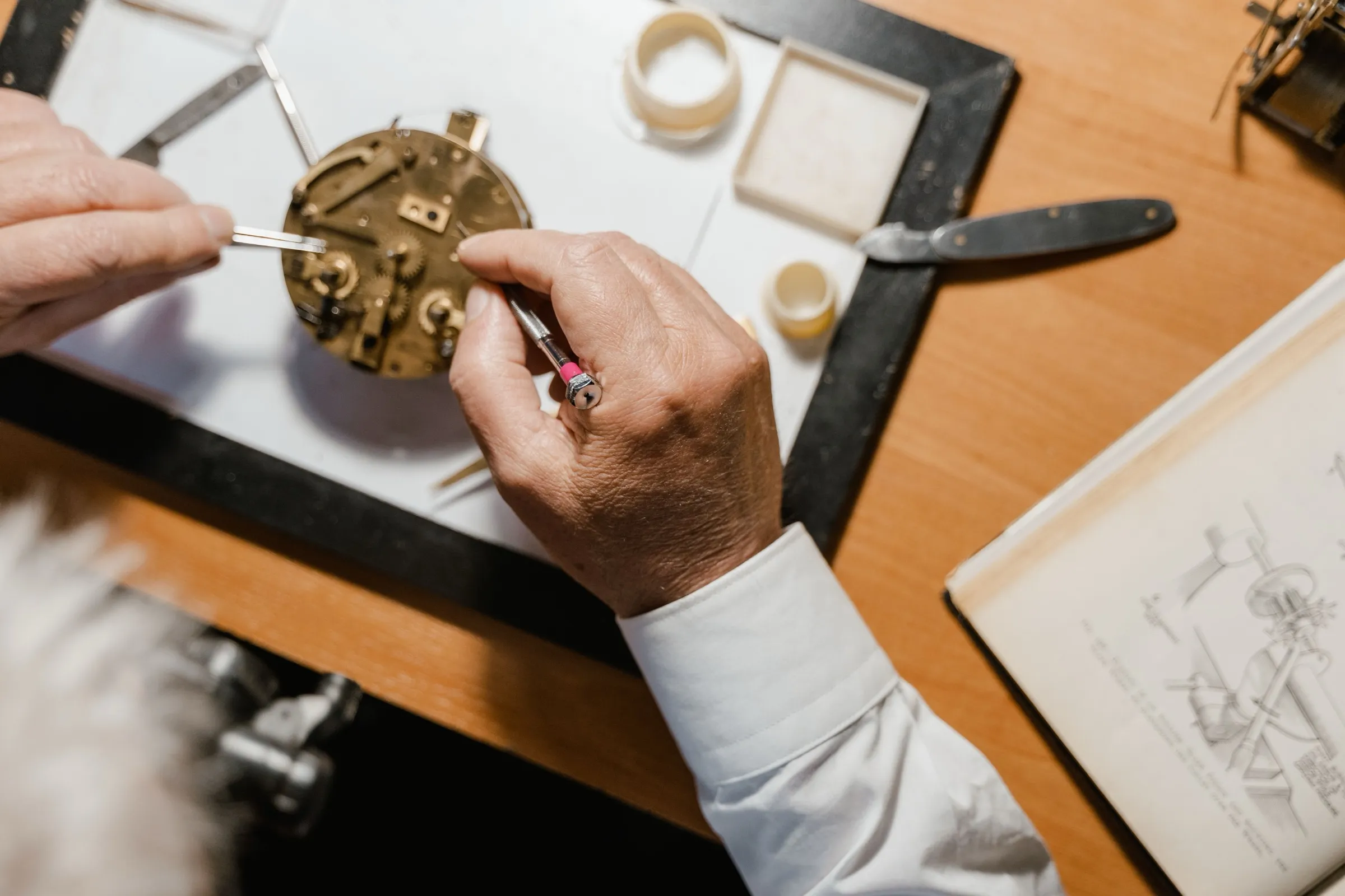 A watchmaker's hands at work over a brass movement on the bench