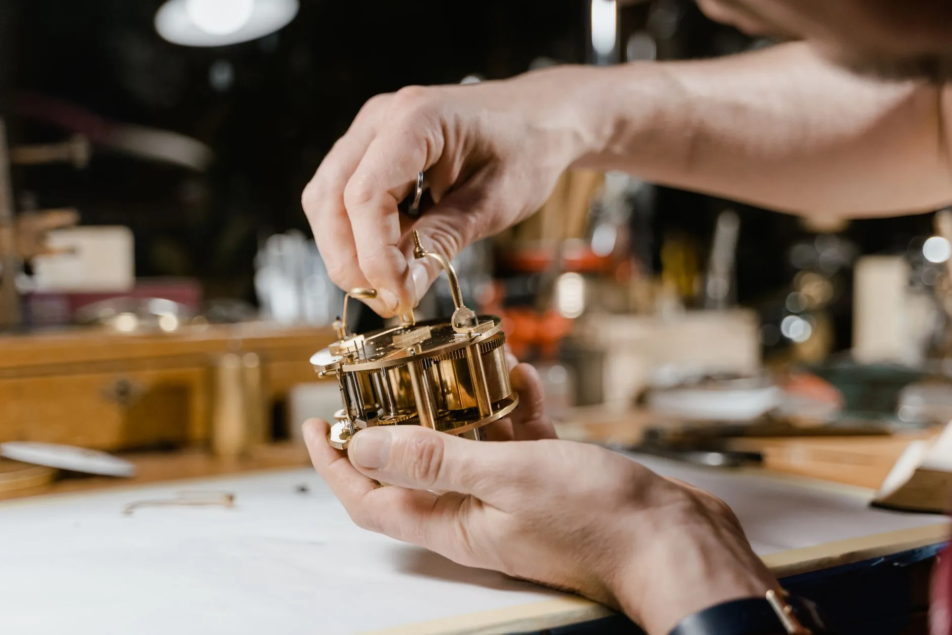 Hands holding a brass clock movement at the bench