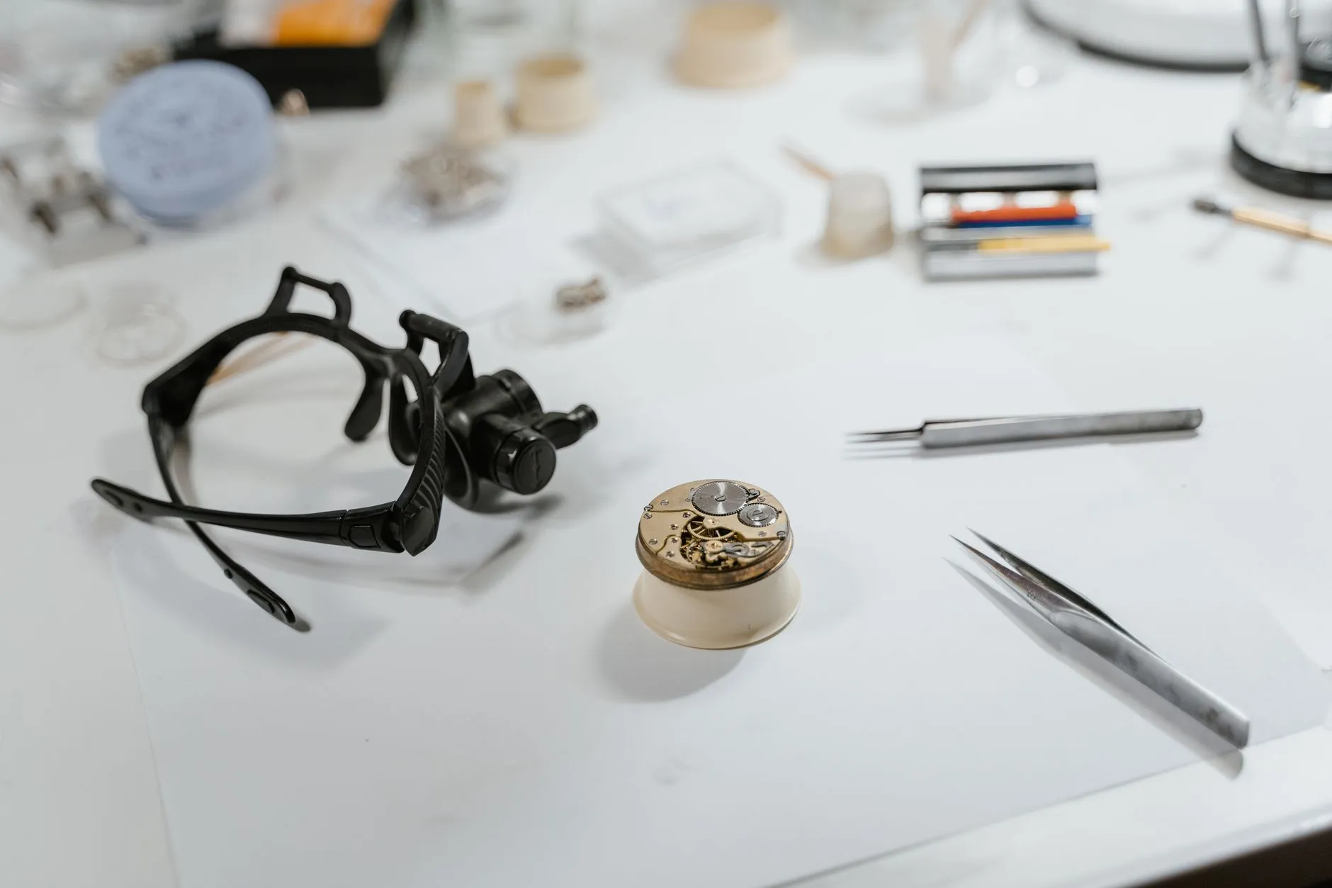 A loupe, tweezers and a movement holder on a white bench mat